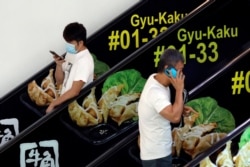 Men, one with a protective mask, use their phones at a mall in Singapore, March 27, 2020.