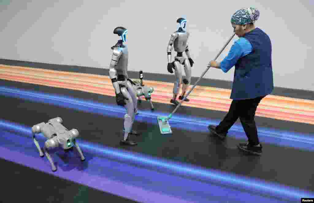 A staff cleans the floor next to robots during Digital Almaty 2025 forum, in Almaty, Kazakhstan.