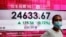 A woman wearing a face mask stands by a bank's electronic board showing the Hong Kong share index at Hong Kong Stock Exchange, Aug. 4, 2020. 