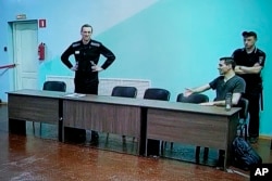 Alexei Navalny, kiri, dan rekannya Daniel Kholodny terlihat di layar TV dalam tautan video yang disediakan oleh Lembaga Pemasyarakatan Federal Rusia, selama sidang di koloni tersebut, di Melekhovo, sekitar 260 kilometer timur laut Moskow, Rusia, 4 Agustus 2023. (Foto: AP)