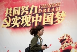 FILE - A woman walks past a billboard promoting the "Chinese Dream," a slogan associated with Chinese President Xi Jinping's ambitions for China, in Beijing, April 5, 2017.