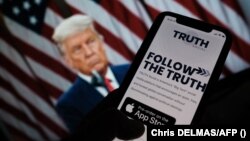 Seseorang sedang melihat aplikasi "Truth Social" di ponsel, dengan foto mantan presiden AS Donald Trump sebagai latar belakang, di Los Angeles, 20 Oktober 2021. (Foto: AFP/ Chris Delmas)