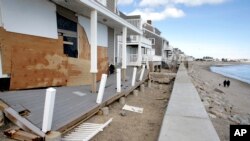People walk along a beach near damaged beachfront homes, March 11, 2018, in Marshfield, Mass. The Northeast is bracing for its third nor'easter in fewer than two weeks. 