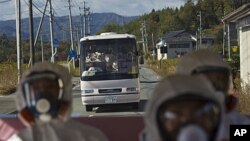 Japanese officials wearing protective suits and masks ride in the back of a bus while a second bus carrying officials and Japanese journalists follow as they drive through the contaminated exclusion zone on their way to the crippled Fukushima Dai-ichi nuc