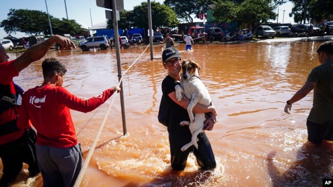 Una mujer carga a un perro mientras camina por una calle inundada después de fuertes lluvias en Porto Alegre, estado de Rio Grande do Sul, Brasil, el lunes 6 de mayo de 2024.