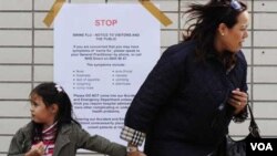 Una mujer pasa con su hija frente a una advertencia contra el virus H1N1 en un hospital de Londres.