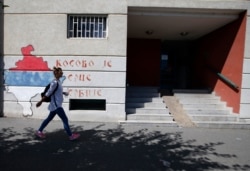 A woman walks past graffiti on a wall reading: "Kosovo is the heart of Serbia," in Belgrade, Serbia, Sept. 4, 2020.