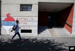 A woman walks past graffiti on a wall reading: "Kosovo is the heart of Serbia," in Belgrade, Serbia, Sept. 4, 2020.