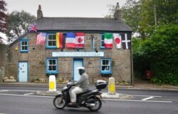 A man rides a motorbike past a pub with flags of the G-7 nations and the flag of Cornwall in St. Ives, Cornwall, England, June 9, 2021.