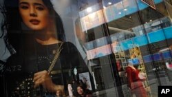 Chinese shoppers are reflected on a fashion boutique's window panels as they walk through the capital city's popular shopping mall in Beijing, Friday, Feb. 1, 2019. 