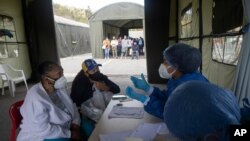 Mujeres escuchan a un trabajador de la salud mientras son examinadas para detectar COVID-19 en un hospital de campaña instalado en el estacionamiento del auditorio Poliedro de Caracas, en Venezuela. Marzo 21, 2021.
