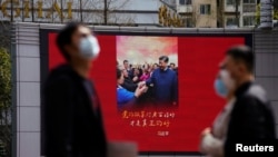 Pedestrians wearing face masks walk past a screen displaying an image of Chinese President Xi Jinping after the city's emergency alert level for coronavirus disease (COVID-19) was downgraded, in Shanghai, China March 23, 2020. REUTERS/Aly Song