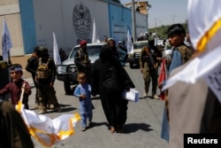Afganistanka sa sinom prolazi između Talibana tokom ceremonije povodom dvije godine od preuzimanja vlasti u Kabulu.