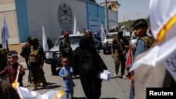 Seorang perempuan Afghanistan bersama anaknya berjalan di antara para pendukung Taliban di jalan Kota Kabul, Afghanistan, di dekat Kedutaan Besar AS pada 15 Agustus 2023. (Foto: Reuters/Ali Khara)