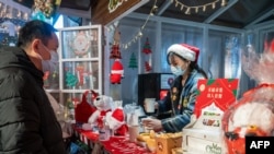 This photo taken on December 24, 2020 shows a vendor offering drinks to a customer at a Christmas-themed market outside of a shopping mall complex on Christmas Eve in Shanghai. (Photo by STR / AFP) / China OUT
