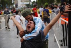 Mourners embrace as they wait to see football star Diego Maradona lying in state outside the presidential palace in Buenos Aires, Argentina, Nov. 26, 2020.