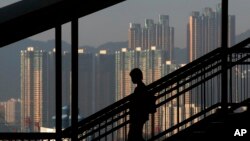 FILE - A woman walks down a stairway against the backdrop of high-rise apartment buildings in Hong Kong.