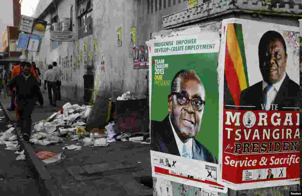 Election campaign posters are pictured near Zimbabweans walking on a street blocked by uncollected garbage in Harare July 17, 2013. President Robert Mugabe&#39;s rivals said the chaotic organisation of early voting for soldiers and police showed Zimbabwe was not ready for the July 31 general election in which nearly six million people had registered to vote.