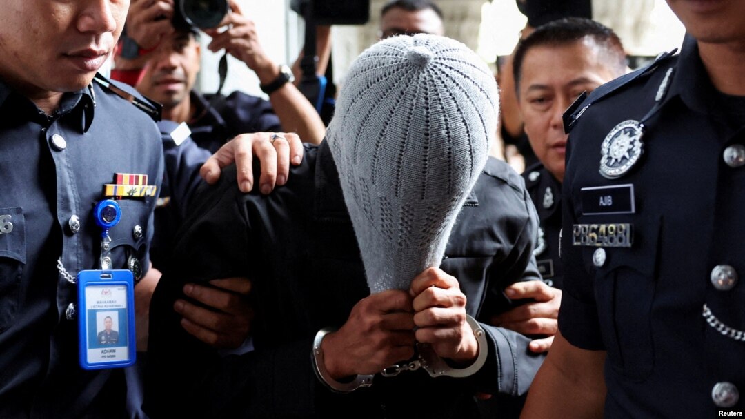 Seorang pria yang terkait dengan Global Ikhwan Service and Business Holdings (GISB) menutupi wajahnya saat dikawal oleh petugas polisi setelah didakwa di pengadilan di Putrajaya, Malaysia, 18 September 2024. (Foto: Reuters)