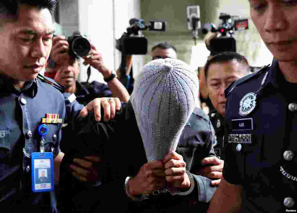 A man linked to Global Ikhwan Service and Business Holdings (GISB) covers his face as he is escorted by police officers after being charged in a court in Putrajaya, Malaysia. GISB allegedly runs the charity homes where suspected child sexual abuse took place.