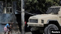 FILE - A woman and a child duck near a police vehicle after leaving school amid gang violence in Port-au-Prince, Haiti, March 3, 2023.