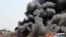 An Iraqi policeman stands near burning vehicles moments after one in a series of bombs hit the Shiite stronghold of Sadr City, in Baghdad, Iraq, killing tens.