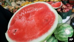 A person holds a cut watermelon at a fruit stand. 