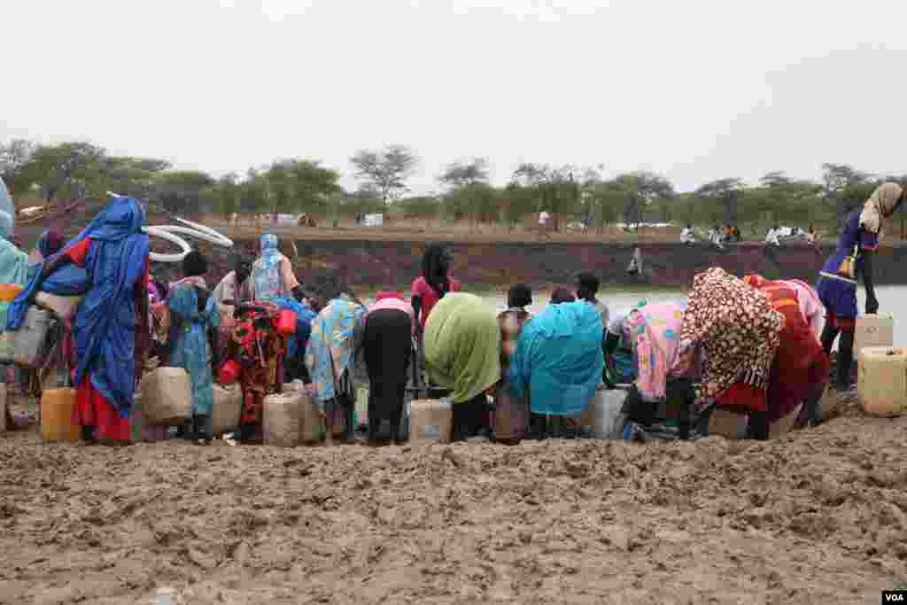 Women who crossed over from Sudan's Blue Nile state with little food or water fill jerry cans at a watering hole called Km 18 on June 20, 2012. Water from watering holes can carry disease. (Hannah McNeish/VOA)
