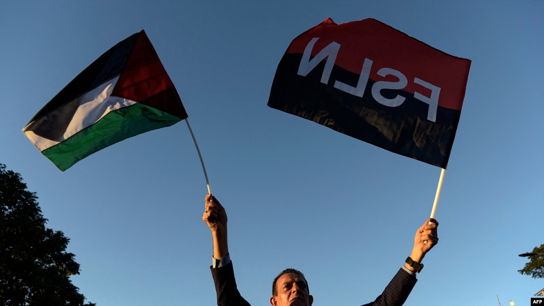 Seorang pria mengacungkan bendera Palestina dan Sandinista saat peresmian jalan Gaza untuk mendukung rakyat Palestina, di pusat Kota Managua yang bersejarah, di Nikaragua, 30 Januari 2024. (Foto: Oswaldo Rivas/AFP)