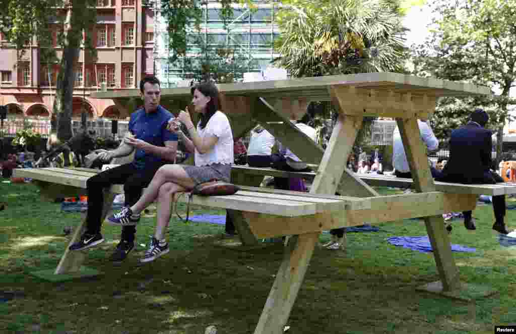 People sit on an oversize picnic table in Soho Square in London.