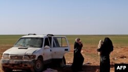 FILE - Two women, wives of an Islamic State fighter who has been identified as a German national, wait to be screened and registered by Syrian Democratic Forces, in the countryside of the eastern Syrian Deir Ezzor province, Jan. 31, 2019.