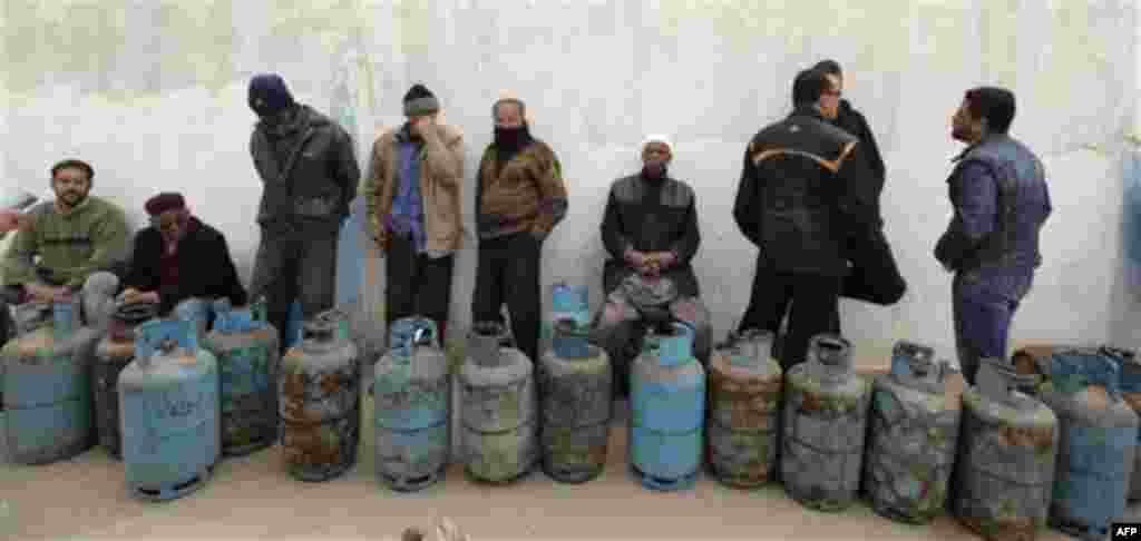 Libyan men wait by empty cooking gas cylinders as they queue in front of a cooking gas storage house in Benghazi, Libya Sunday, March 13, 2011. Libyans queue during the day in Benghazi for cooking gas in front of storage houses that suffer severe shortage