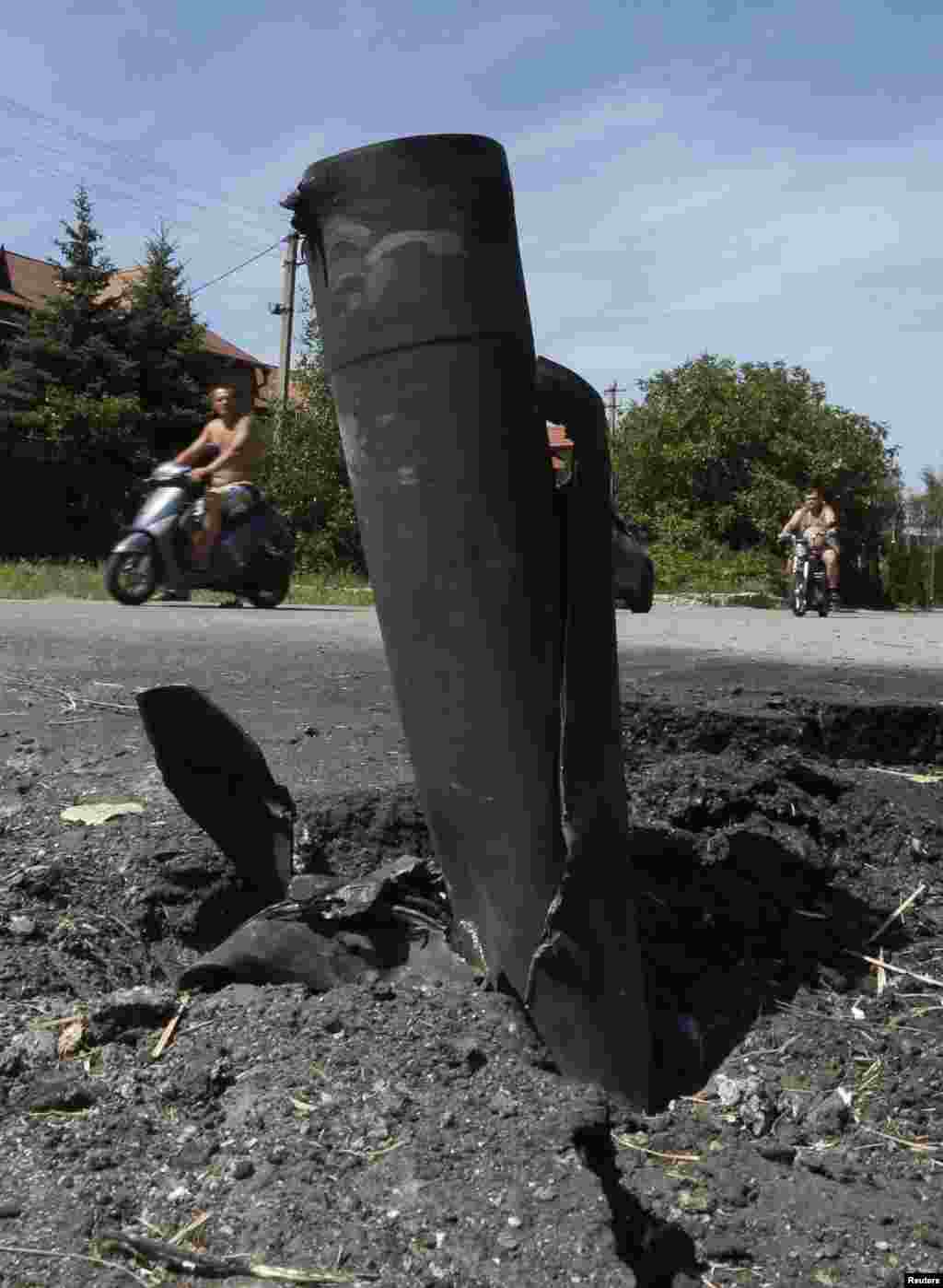 People ride motorcycles past spent ammunition, in the suburbs of Donetsk, July 29, 2014.