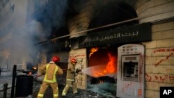 FILE - Firefighters extinguish a fire at a branch of the Credit Libanais Bank that was burnt by anti-government protesters, in the northern city of Tripoli, Lebanon, April 28, 2020.