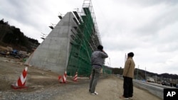 FILE - Local residents look at the 12.5-meter (41-foot)-high concrete barrier under construction in the northern fishing port of Osabe, in Rikuzentakata, Iwate Prefecture, northeastern Japan, March 12, 2015.