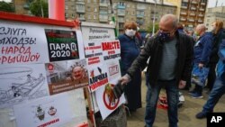FILE - A man uses a slipper to slap a poster that shows a portrait of Belarusian President Alexander Lukashenko as people gather signatures in support of potential presidential candidates in upcoming presidential elections in Minsk, Belarus, May 24, 2020.