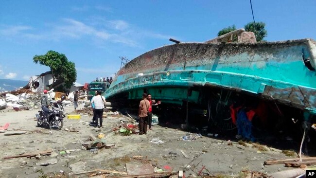 Habitantes observan un barco que fue arrastrado a la costa por el tsunami que asoló el área de Palu, en la provincia de Sulawesi Central en Indonesia, el domingo 30 de septiembre de 2018.