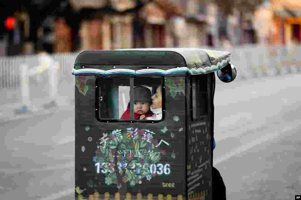 A woman and a toddler ride a tricycle taxi on a street in Beijing, China.