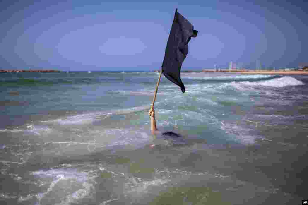 A man waves a black flag in the water during a protest against government&#39;s decision to close beaches during the three-week nationwide lockdown due to the coronavirus pandemic,in Tel Aviv, Israel, Sept 19, 2020.