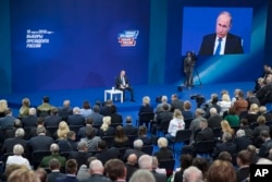 Russian President Vladimir Putin, sitting on the stage at centre rear, speaks to his supporters during a meeting for his campaign in Moscow, Jan. 30, 2018.