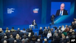 FILE - Russian President Vladimir Putin, sitting on the stage at center rear, speaks to his supporters during a meeting for his campaign in Moscow, Jan. 30, 2018. 