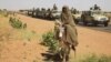 A government convoy passes a woman on a donkey in Tabit in North Darfur on Nov. 20, 2014. Human Rights Watch says Sudanese forces raped scores of women in the village last year. (AP/Abd Raouf)