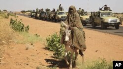 A government convoy passes a woman on a donkey in Tabit in North Darfur on Nov. 20, 2014. Human Rights Watch says Sudanese forces raped scores of women in the village last year. (AP/Abd Raouf)