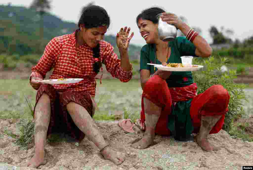 Dua petani beristirahat untuk makan siang sambil merayakan Hari Padi Nasional, yang juga disebut Asar Pandra, untuk menandai dimulainya musim tanam padi di sawah ketika musim hujan tiba, di Kathmandu, Nepal.&nbsp;