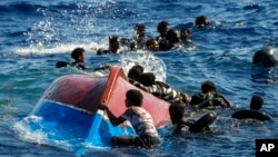 FILE - Migrants swim next to their overturned wooden boat during a rescue operation by Spanish NGO Open Arms at south of the Italian Lampedusa island in the Mediterranean Sea, Aug. 11, 2022. 