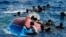 FILE - Migrants swim next to their overturned wooden boat during a rescue operation by Spanish NGO Open Arms at south of the Italian Lampedusa island in the Mediterranean Sea, Aug. 11, 2022. 