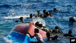 FILE - Migrants swim next to their overturned wooden boat during a rescue operation by Spanish NGO Open Arms at south of the Italian Lampedusa island in the Mediterranean Sea, Aug. 11, 2022. 