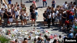 People form a circle around flowers placed on the road in tribute to victims of the truck attack along the Promenade des Anglais on Bastille Day that killed scores and injured as many in Nice, France, July 17, 2016.