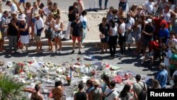 People form a circle around flowers placed on the road in tribute to victims of the truck attack along the Promenade des Anglais on Bastille Day that killed scores and injured as many in Nice, France, July 17, 2016. 