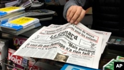 A newsstand owner picks up a copy of the satirical newspaper Le Canard enchaine, or "The Chained Duck" in Paris, Feb. 1, 2017. The dirt-digging weekly claims that conservative presidential candidate Francois Fillon's political clout helped secure handsomely paid jobs for his wife and two of their children.